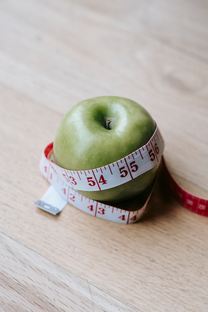 A green apple encircled by a measuring tape, symbolizing diet and fitness goals.